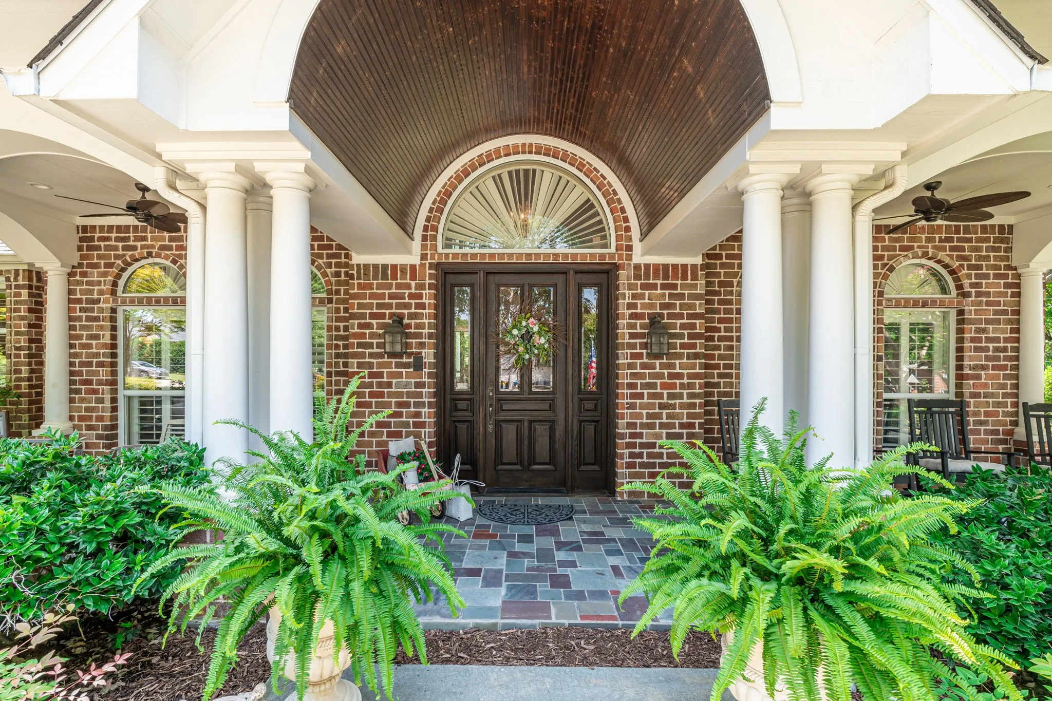 Brick exterior with a covered porch featuring multiple white columns, a dark wood-finish double entry door, and an arched transom window