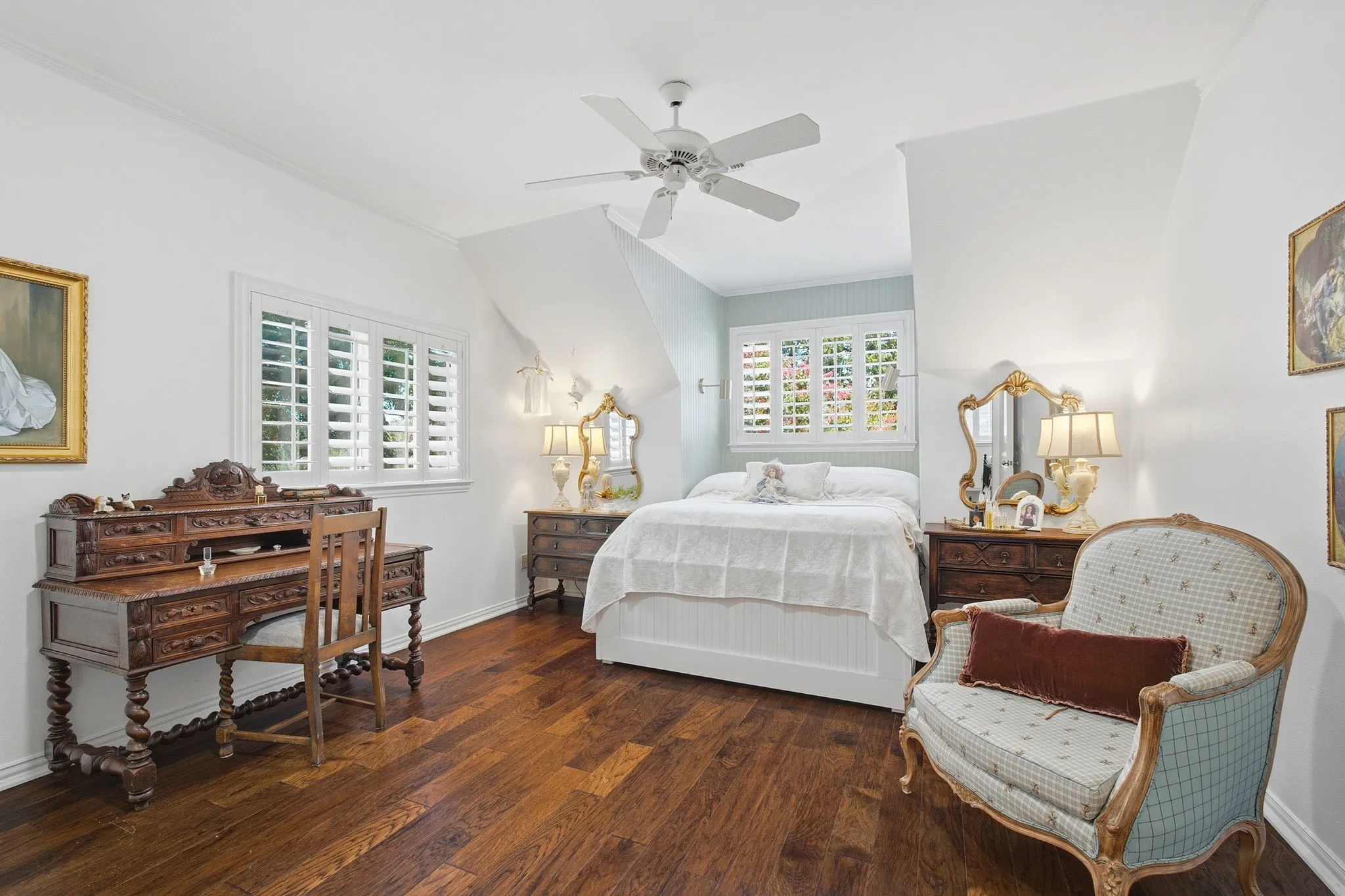 Spacious primary bedroom featuring hardwood flooring, ceiling fan, and abundant natural light from multiple shuttered windows