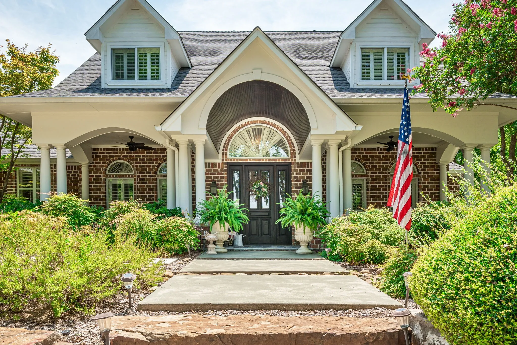 Elegant brick and cream exterior showcasing a grand arched entryway with transom window, flanked by classical columns and dual dormers