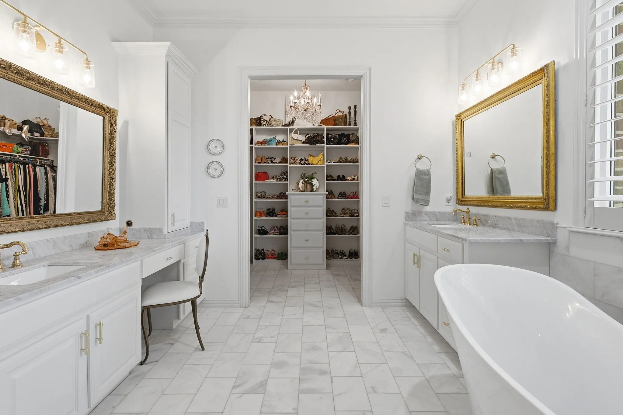 Spa-inspired primary bathroom featuring a freestanding soaking tub, dual vanities with marble countertops and gold-framed mirrors, polished chrome fixtures, and geometric tile flooring