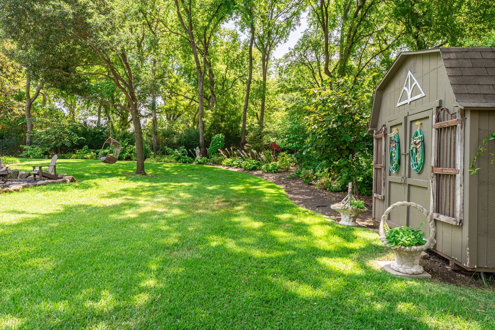 Expansive green lawn with mature trees, established landscaping, and a detached storage shed featuring a gable roof