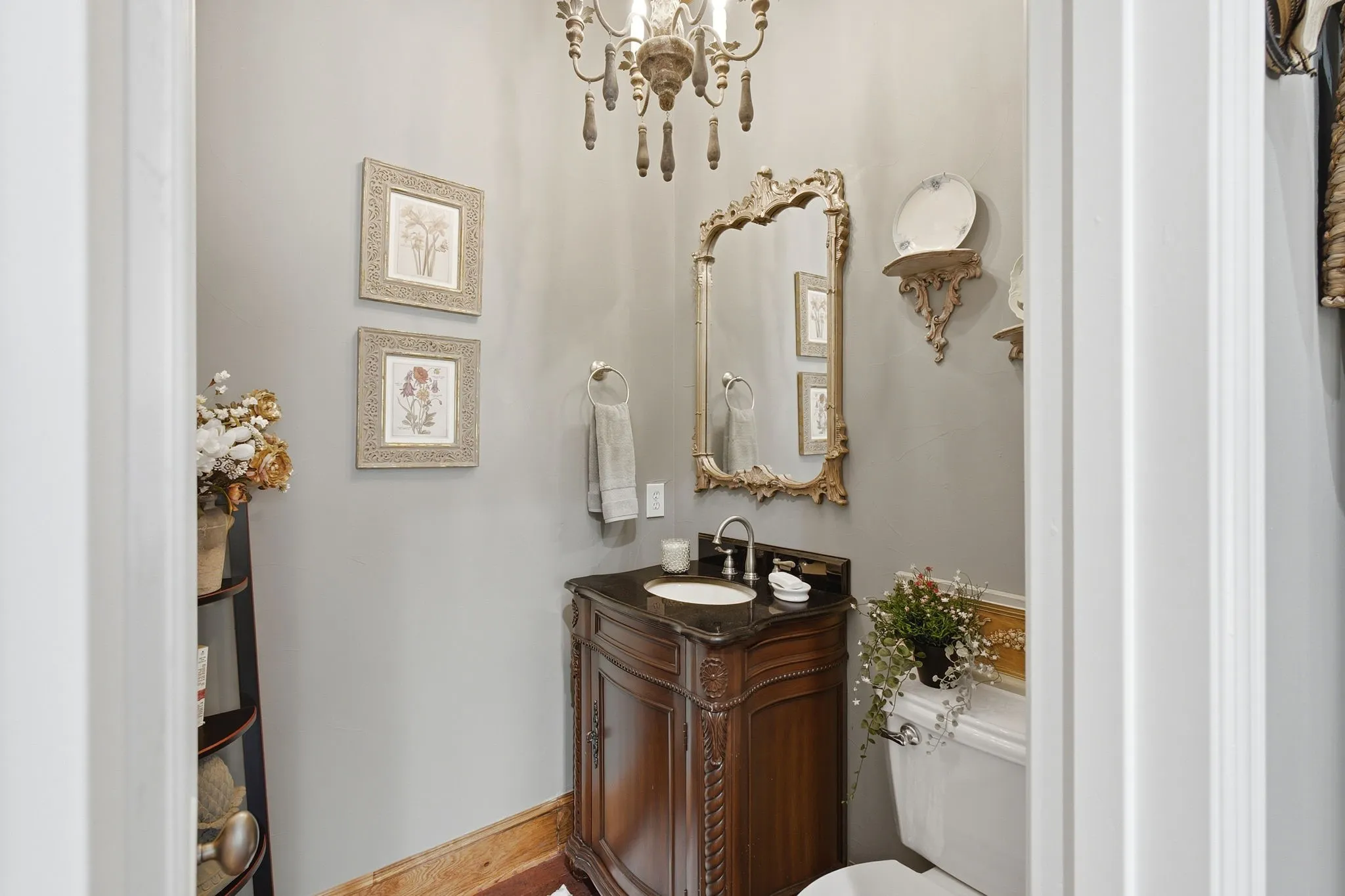Elegant powder room featuring a wood-finish vanity with carved detailing, dark countertop, and brass-accented mirror