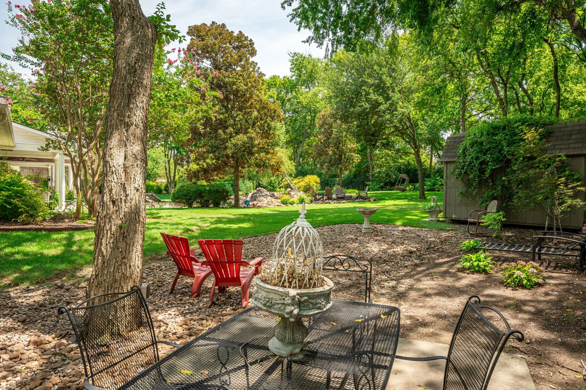 Expansive landscaped yard featuring mature trees, a storage shed, and a concrete patio with gravel perimeter