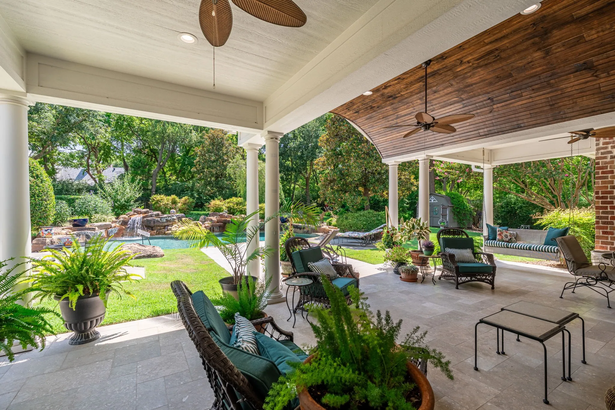 Expansive covered patio with wood-beam ceiling and ceiling fan, featuring concrete flooring and multiple support columns