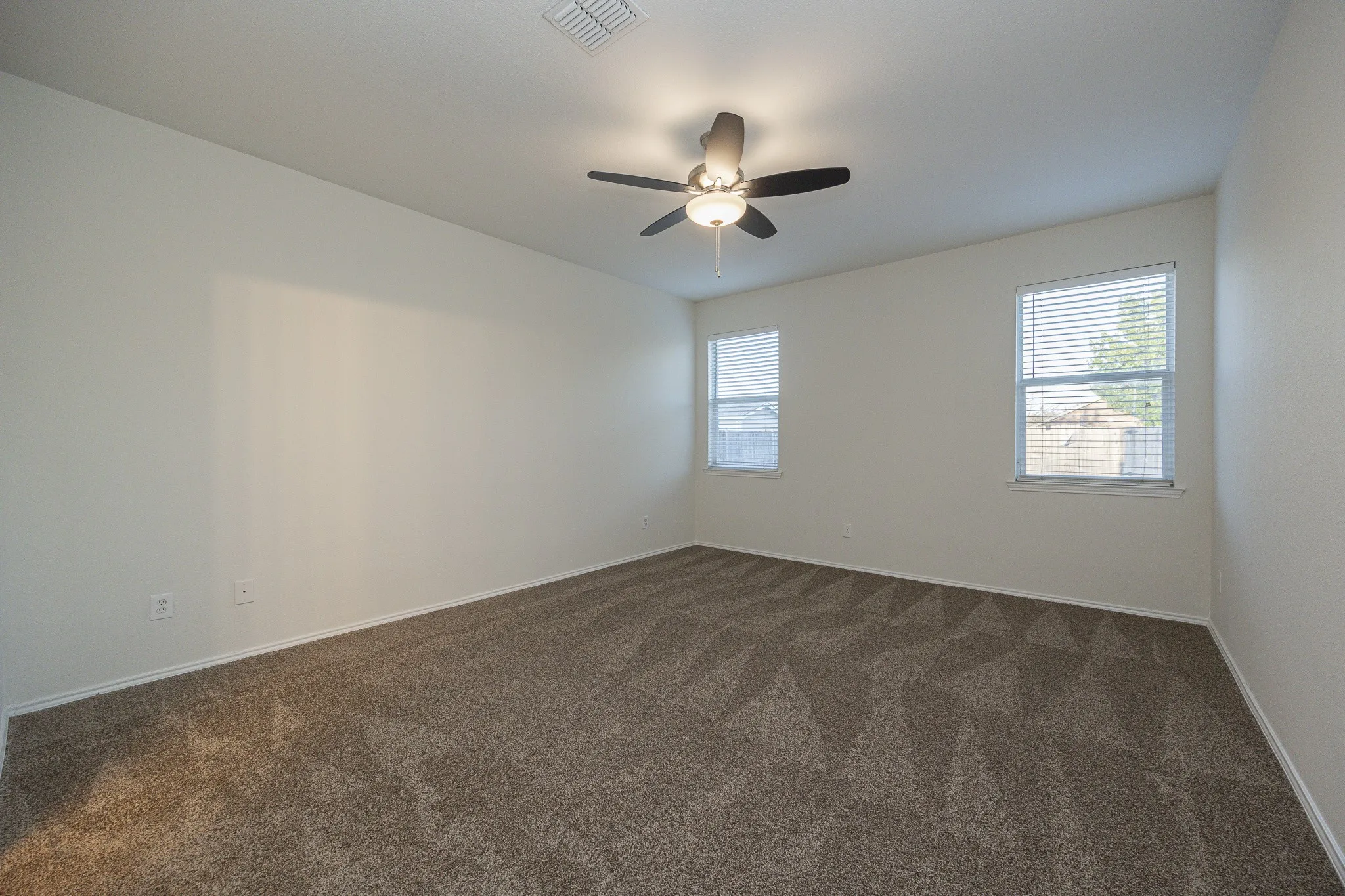 Spacious room with plush patterned carpeting, multiple windows with blinds, and a ceiling fan with integrated lighting