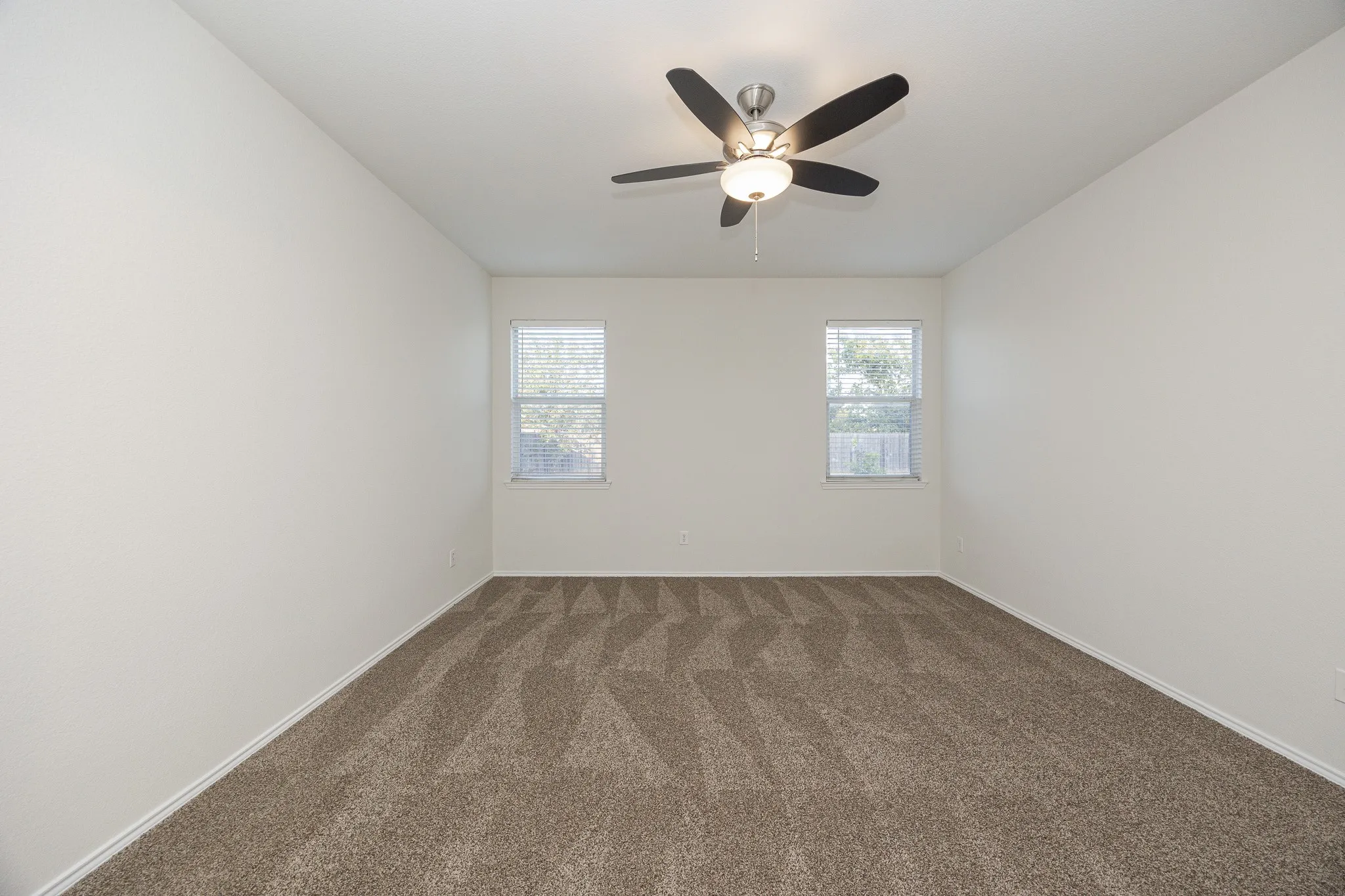 Neutral-toned walls, textured carpeting, contemporary ceiling fan with integrated lighting, and two windows with blinds