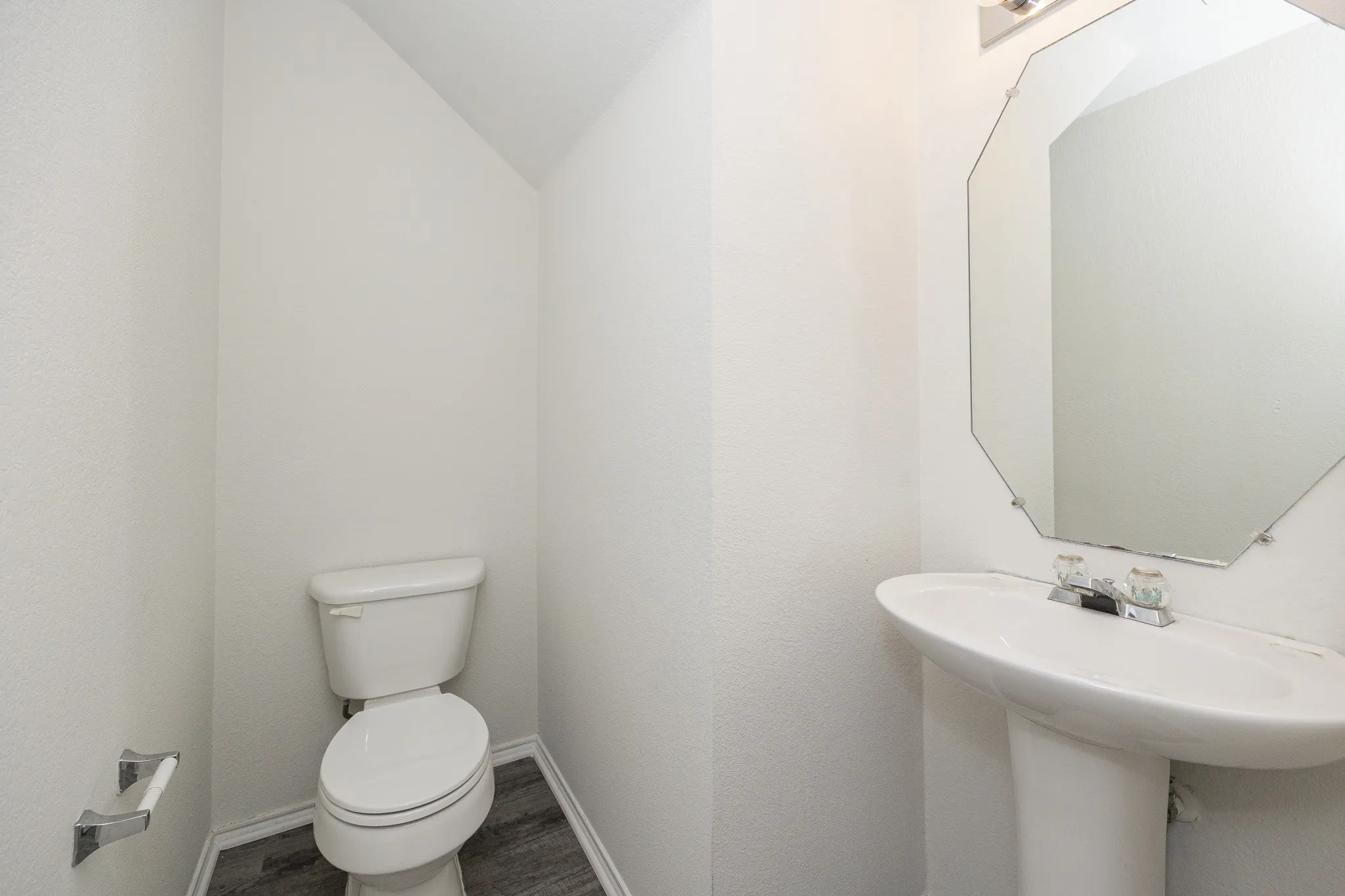 Compact half bath featuring a ceramic toilet, pedestal sink, and octagonal framed mirror