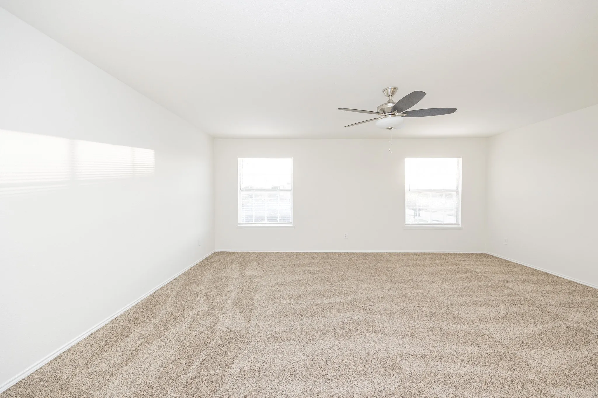 Spacious bedroom with neutral carpet flooring, two windows providing natural light, and a ceiling fan for air circulation