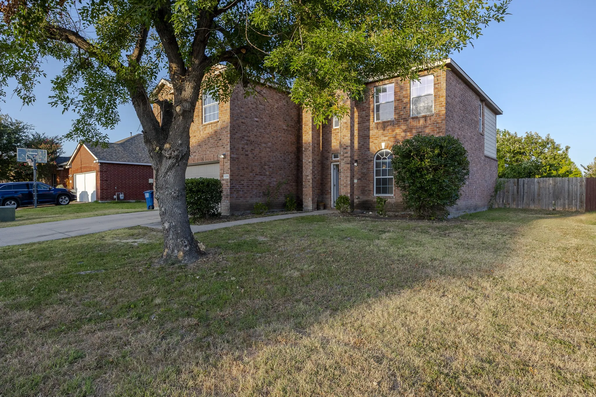 Brick exterior with an attached garage, arched window, and mature front yard tree