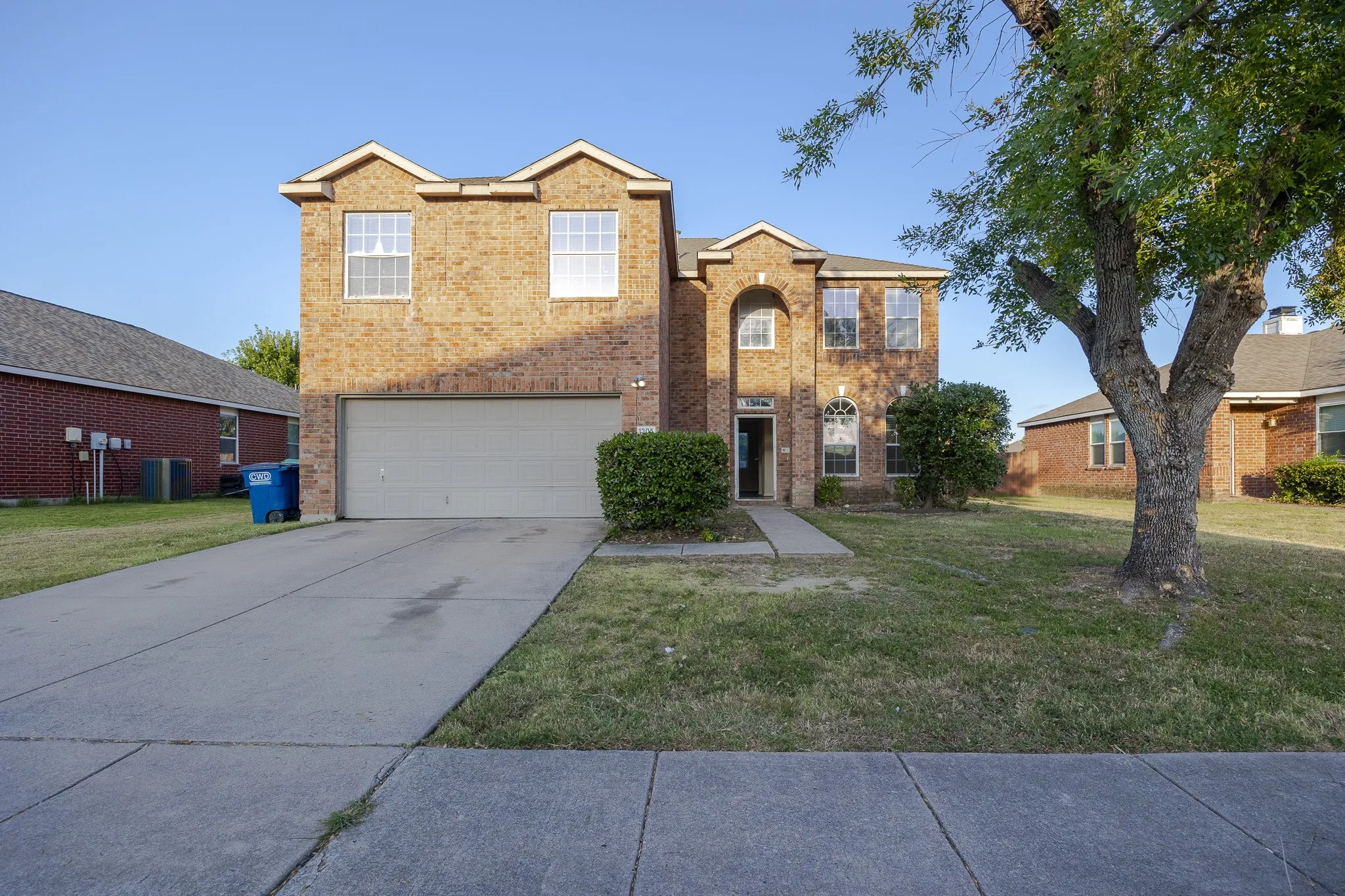 Brick two-story home featuring a two-car garage, manicured front lawn, and mature landscaping