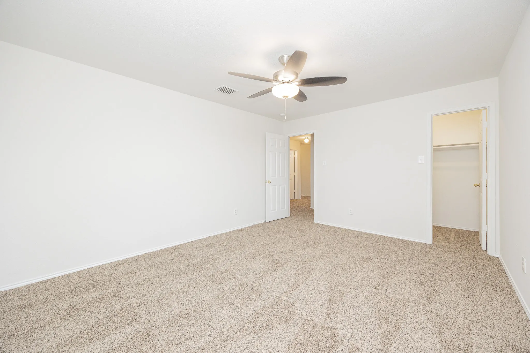 Carpeted flooring, ceiling fan with integrated lighting, neutral wall palette, and built-in closet shelving