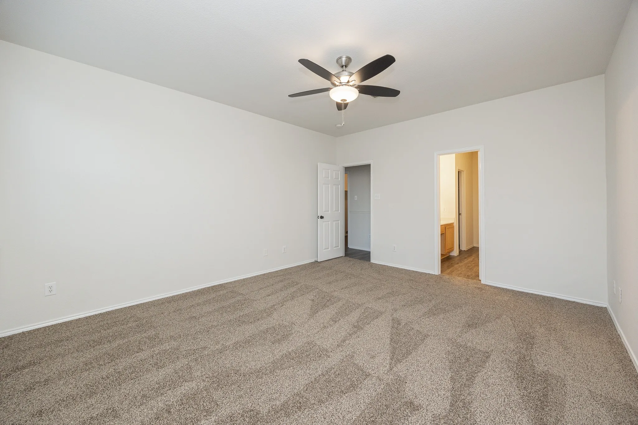 Spacious room featuring neutral carpeting, a ceiling fan with integrated lighting, and white walls