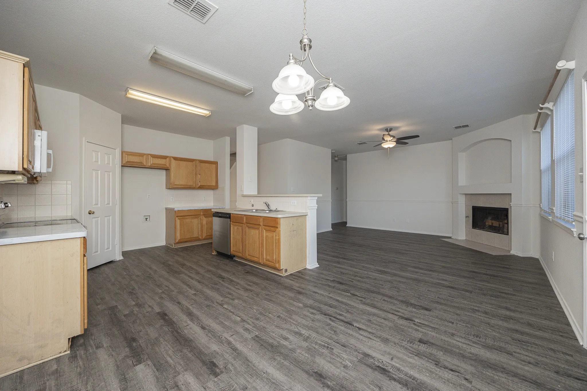 Open-concept living and kitchen area featuring wood-finish cabinetry, a central island with seating space, dark wood-finish flooring throughout, and abundant natural lighting from multiple windows