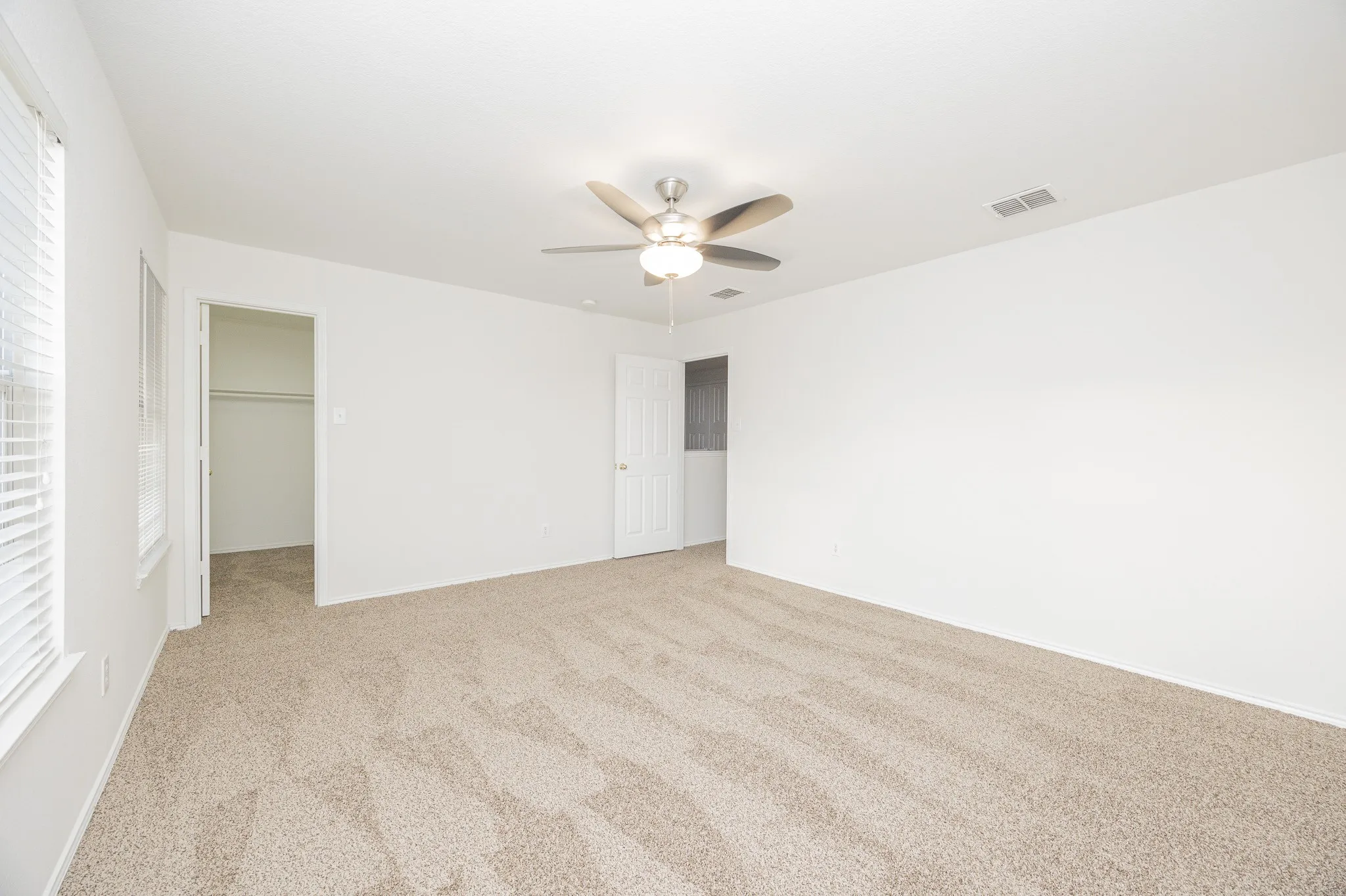 Neutral tone carpeting, white walls, and a ceiling fan with integrated lighting