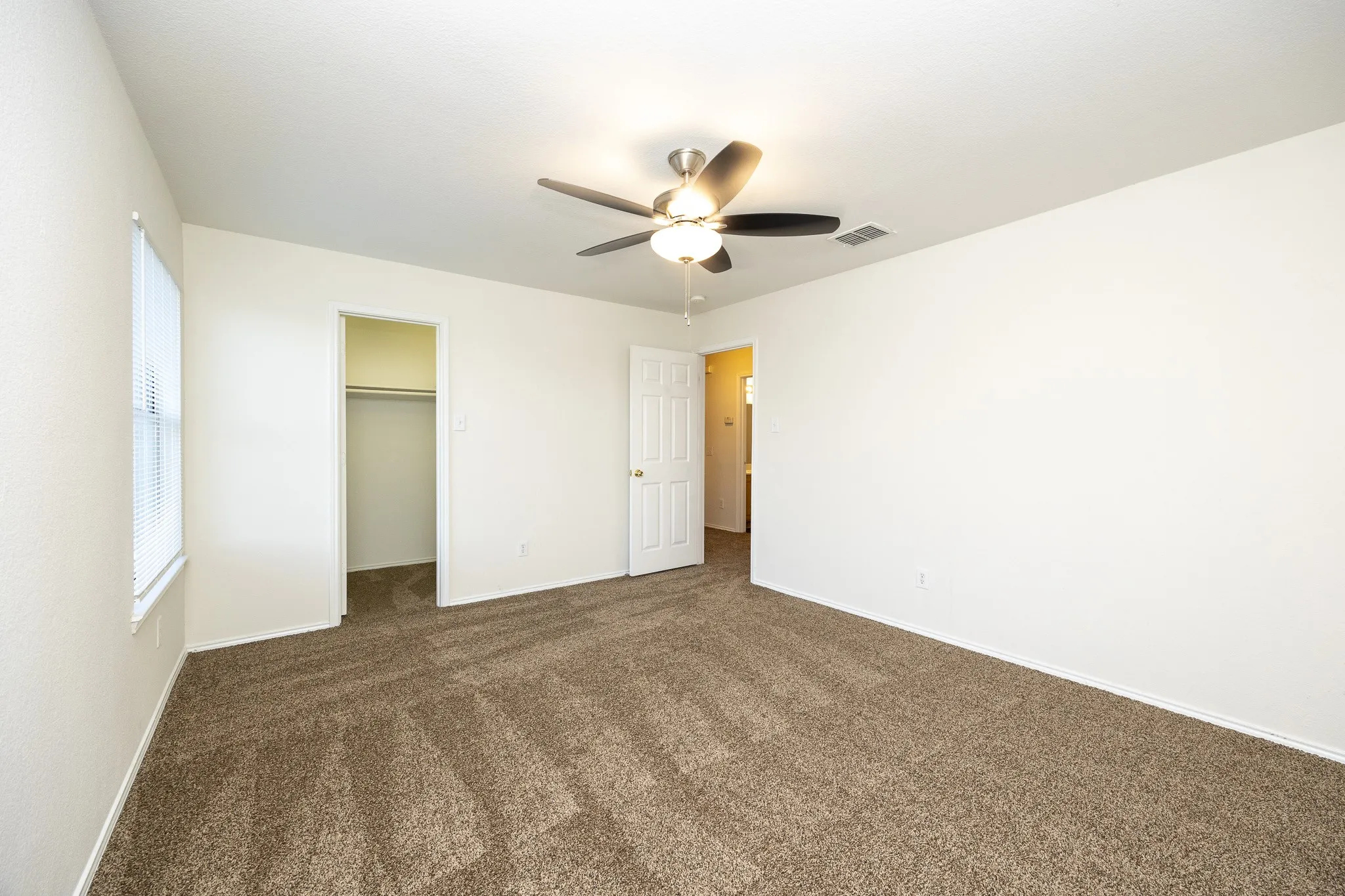 Spacious interior with neutral-toned carpeting, a ceiling fan with integrated lighting, window with blinds, and a closet with hanging rod