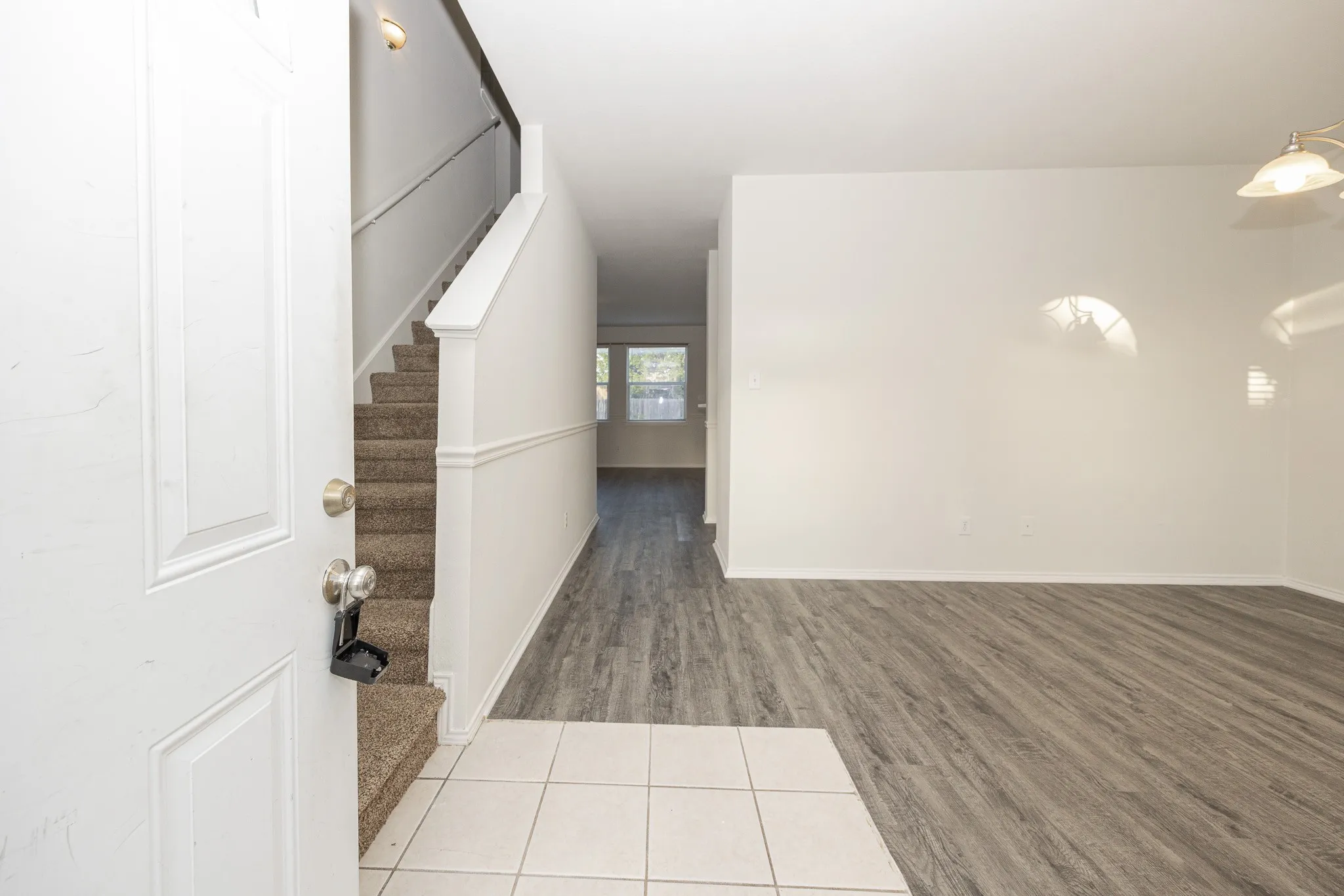Entryway featuring a white paneled door, ceramic tile flooring, wood-finish flooring, and a carpeted staircase with a white railing