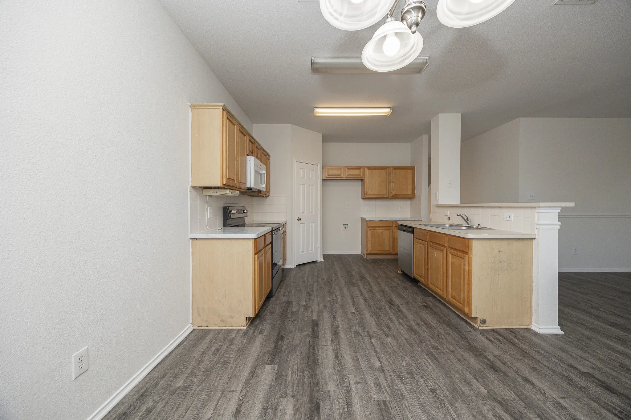 Wood-finish flooring, light wood cabinetry, stainless steel appliances, white countertops, and a built-in microwave