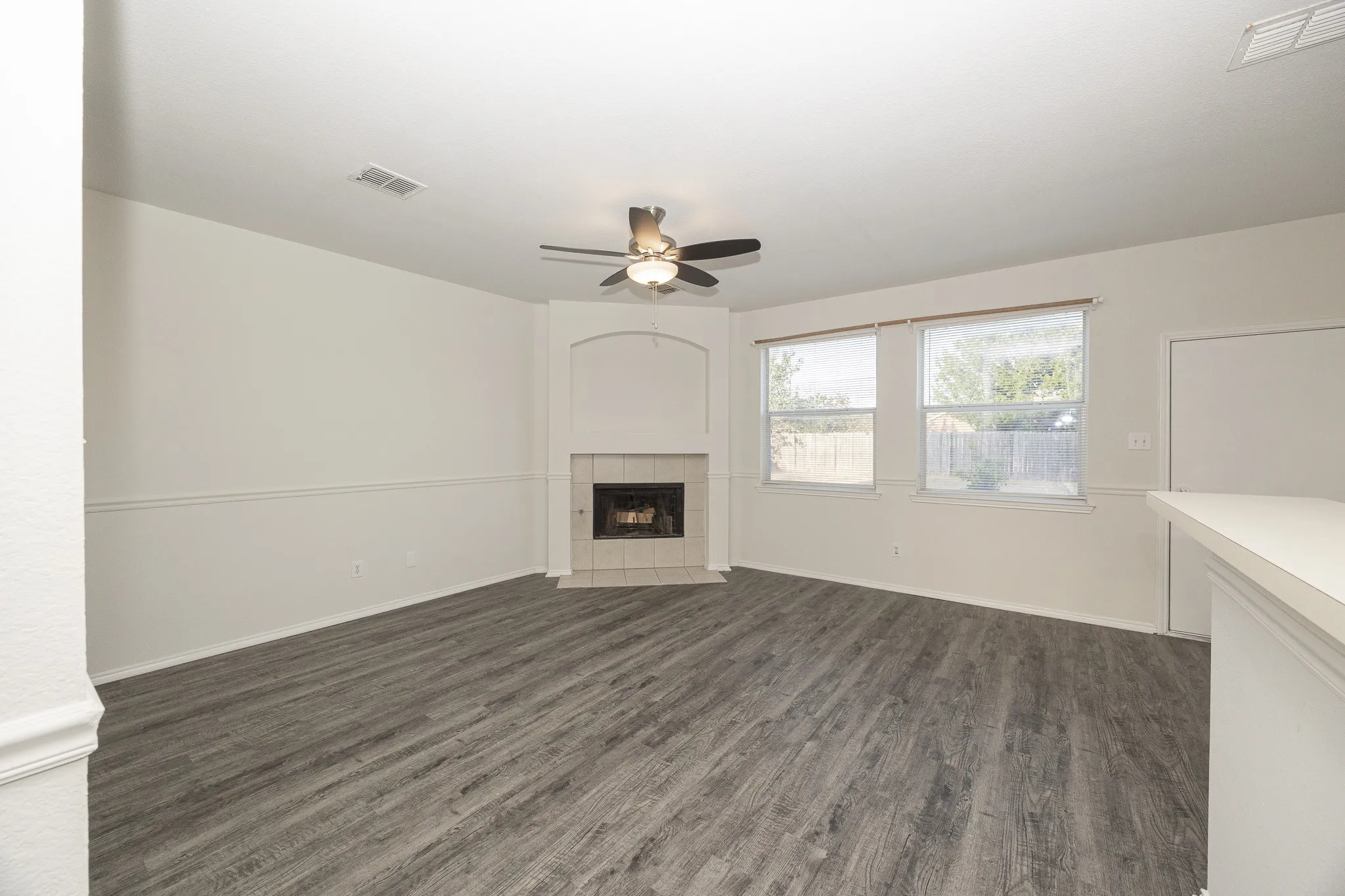 Wood-finish flooring, corner fireplace with tile surround, ceiling fan, and multiple windows