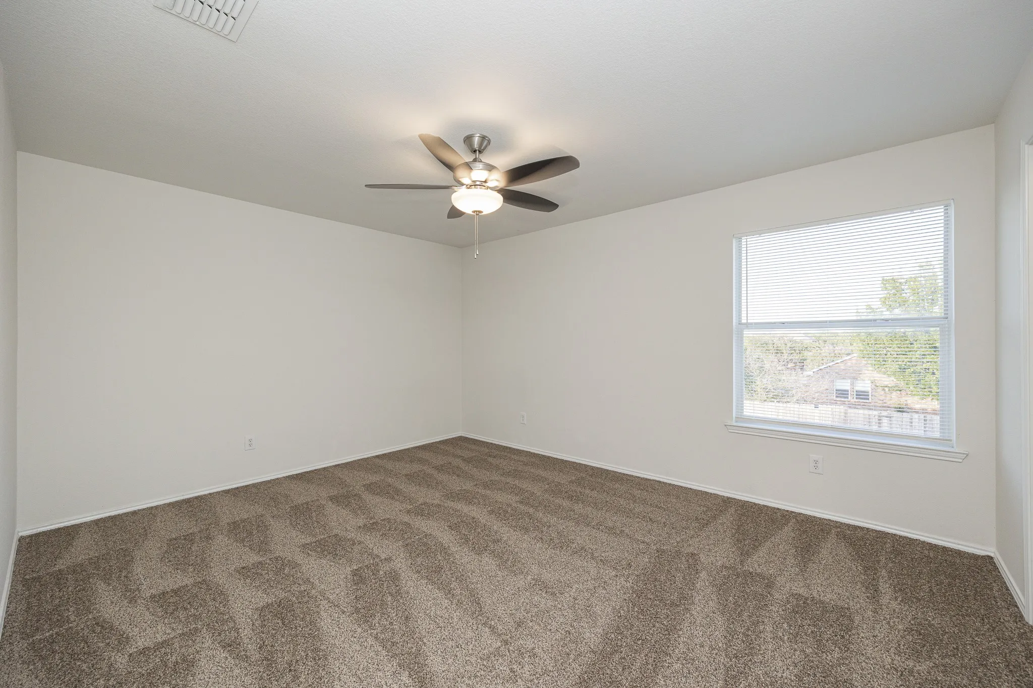 Neutral wall finishes with a single window, ceiling fan with integrated lighting, and patterned carpet flooring