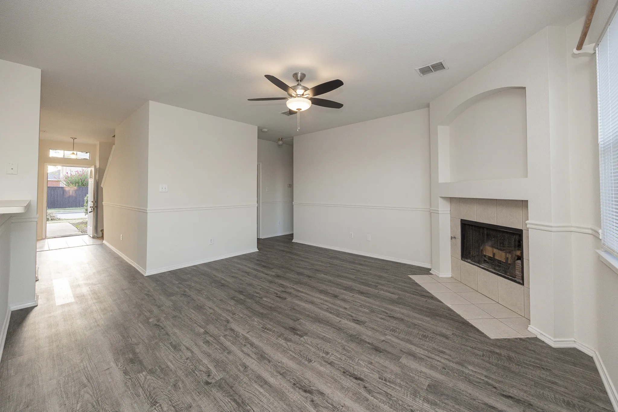 Spacious living area featuring wood-finish flooring, a ceiling fan, and a fireplace with a tiled hearth
