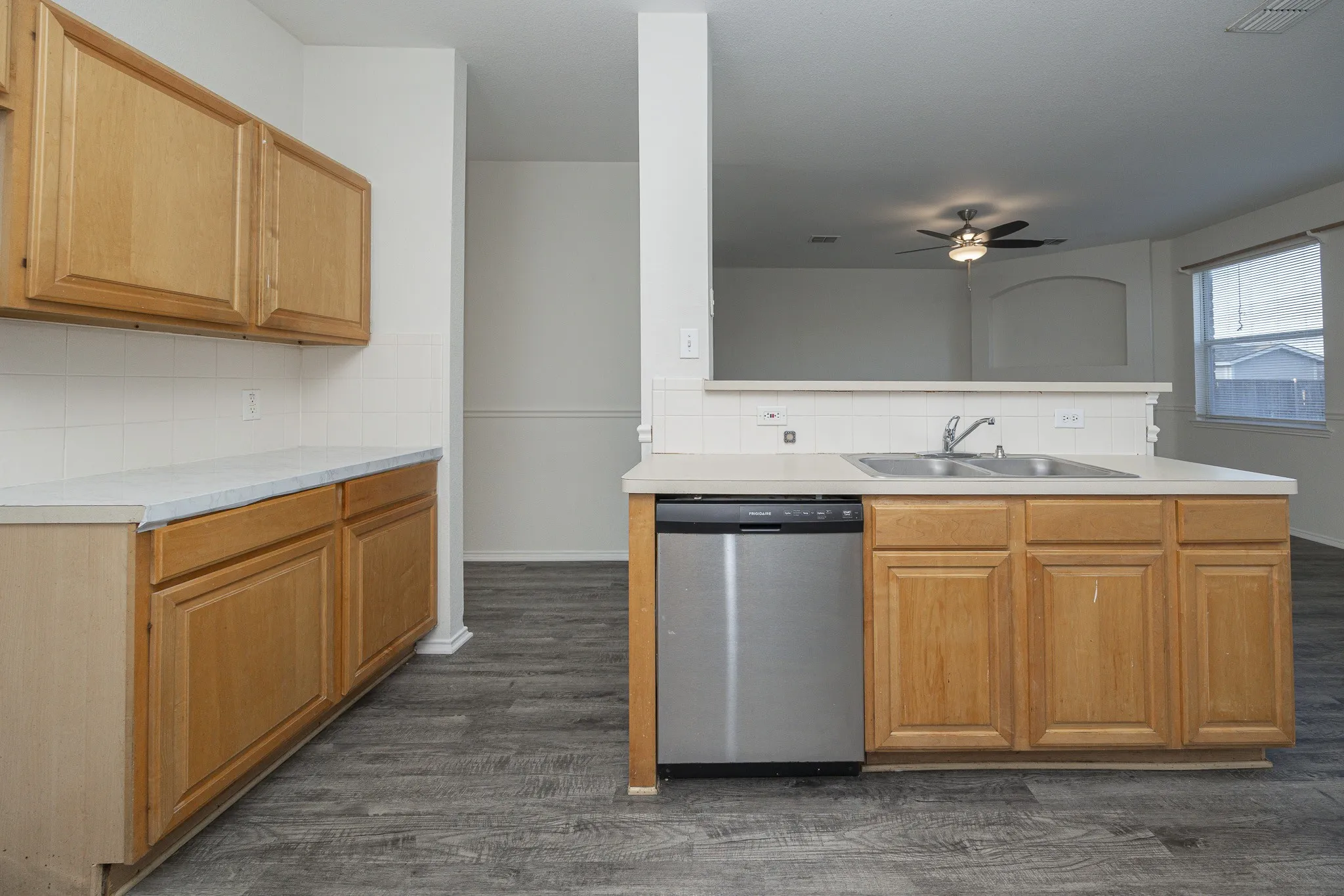 Spacious kitchen featuring wood-finish cabinetry, stainless steel dishwasher, laminate countertops, and a center island with sink