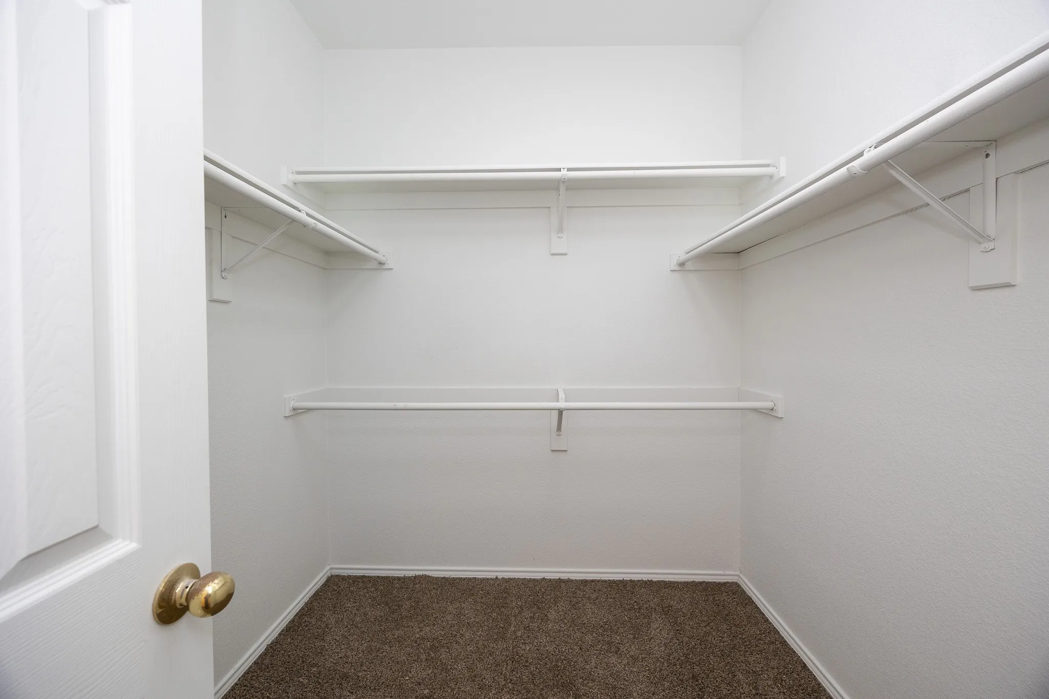 Spacious closet with white wire shelving, hanging rods, and neutral-toned carpeting