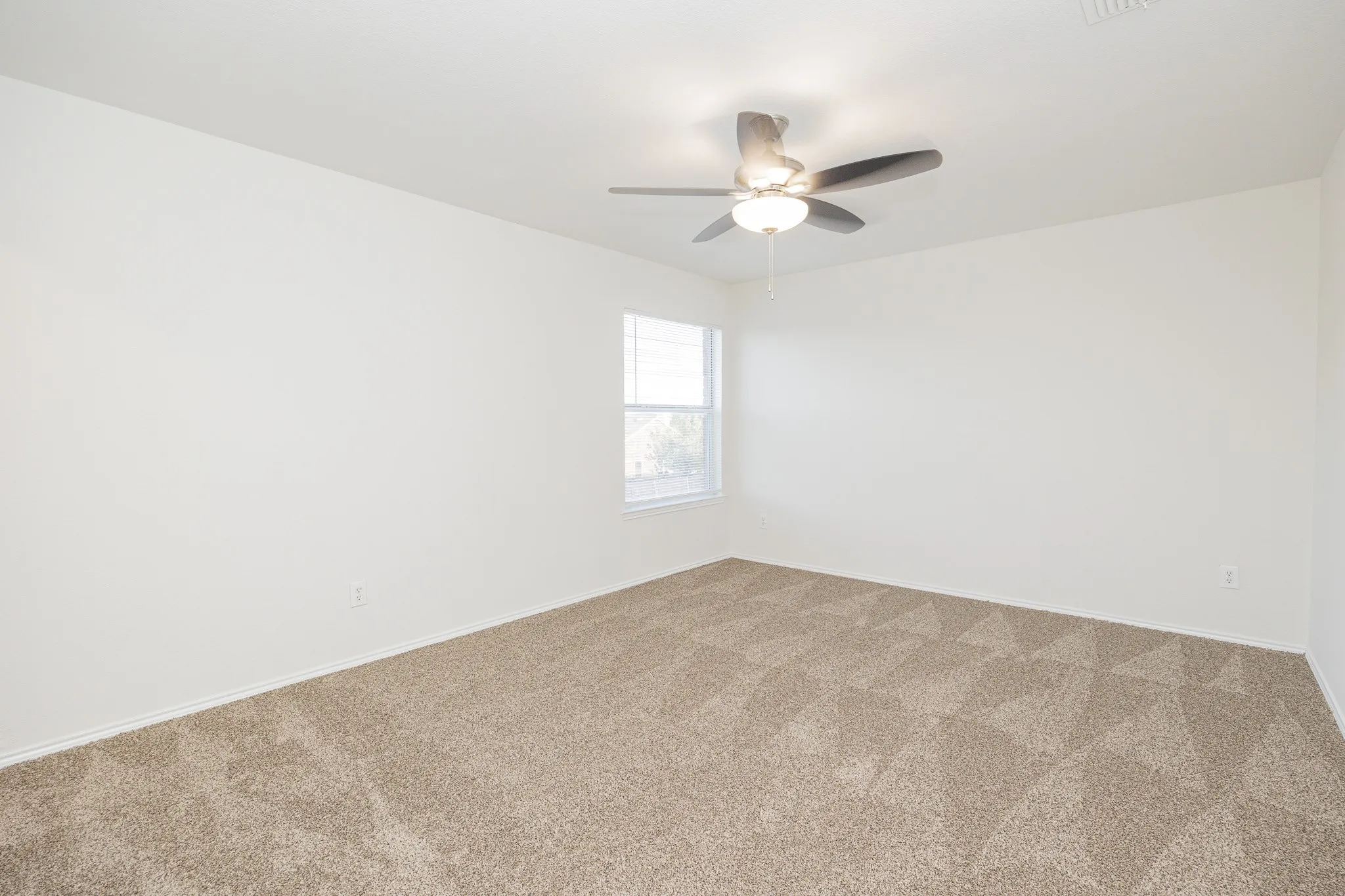 Neutral-toned wall paint, patterned carpeting, ceiling fan with integrated lighting, and a window providing natural illumination