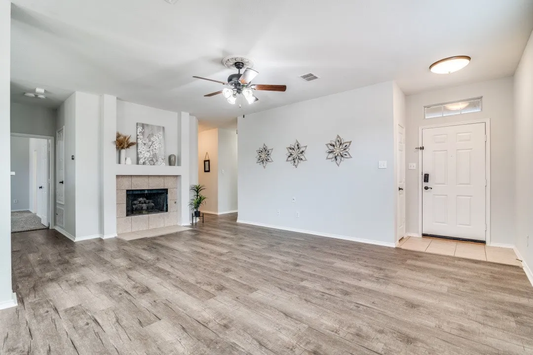 Wood-finish flooring throughout, ceiling fan with integrated lighting, recessed fireplace with tile surround, white entry door with transom window, and flush mount ceiling light fixture