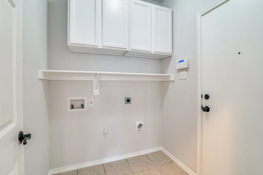 Laundry area with white shaker-style cabinetry, a white storage shelf, and tile flooring