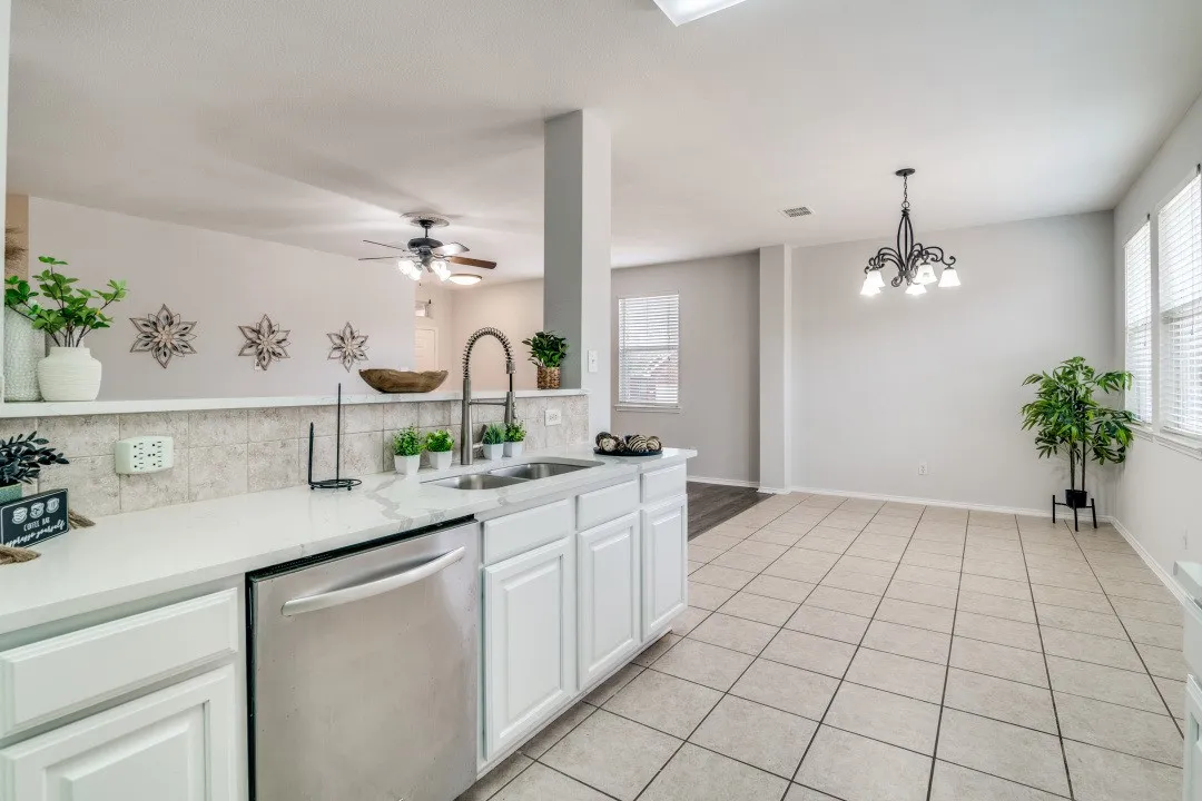 Stainless steel dishwasher, single basin sink with a gooseneck faucet, white cabinetry, light-toned countertop, and tiled flooring