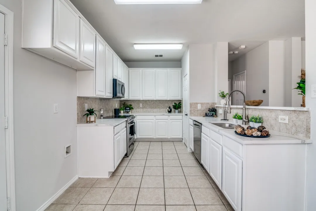 White cabinetry, stainless steel appliances, tile flooring, stone countertops, and a tile backsplash