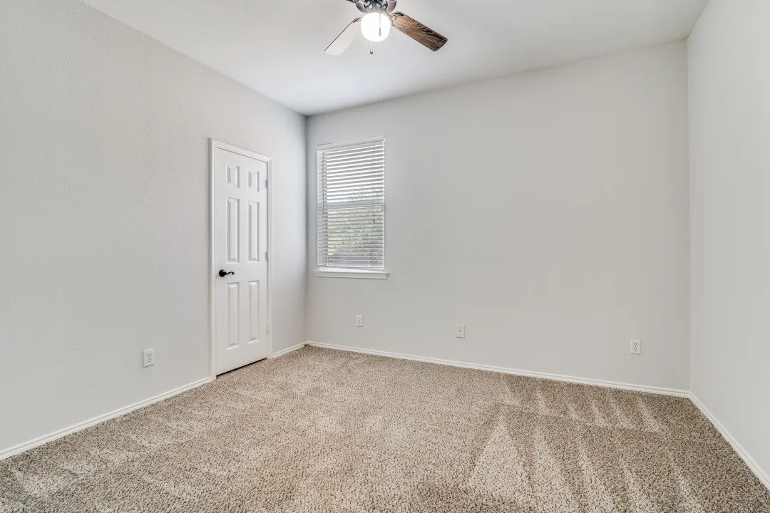 Neutral wall tones, textured carpeting, window with blinds, and a ceiling fan