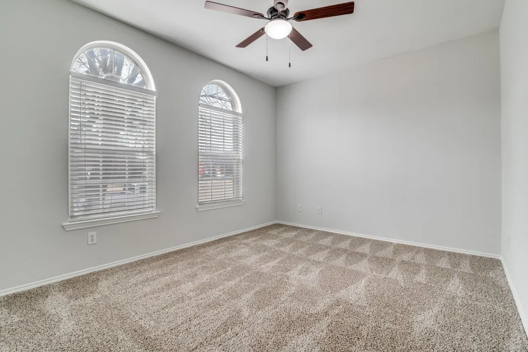 Arched windows, neutral wall tones, textured carpet, and a ceiling fan with integrated lighting