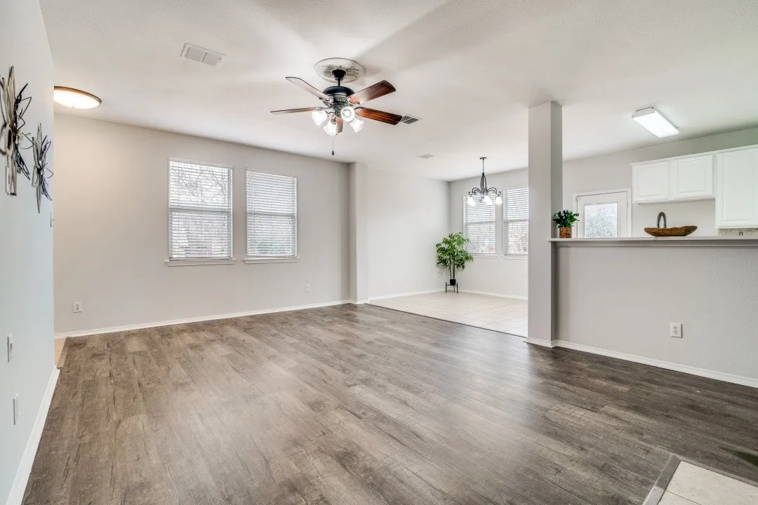 Wood-finish flooring, multiple windows with blinds, ceiling fan with integrated lighting, recessed lighting, and a breakfast bar with white cabinetry