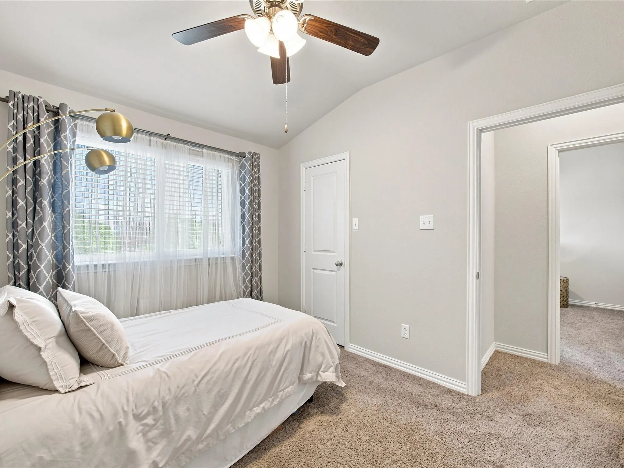 Vaulted ceiling with a ceiling fan, window with blinds and sheer curtains, carpeted flooring, and a white interior door