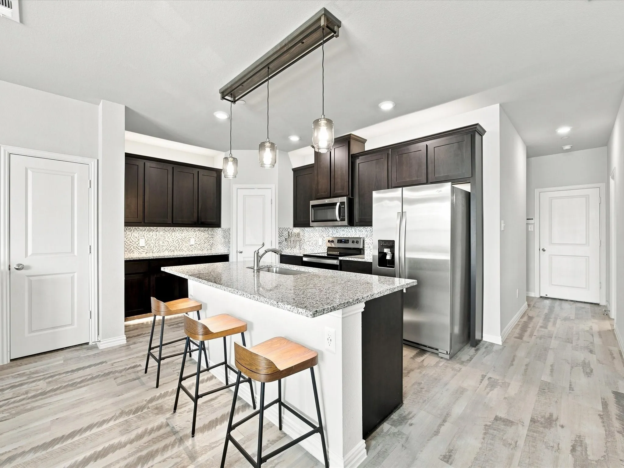 Kitchen featuring dark wood cabinetry, a granite-topped island, stainless steel appliances, a mosaic tile backsplash, and wood-finish flooring