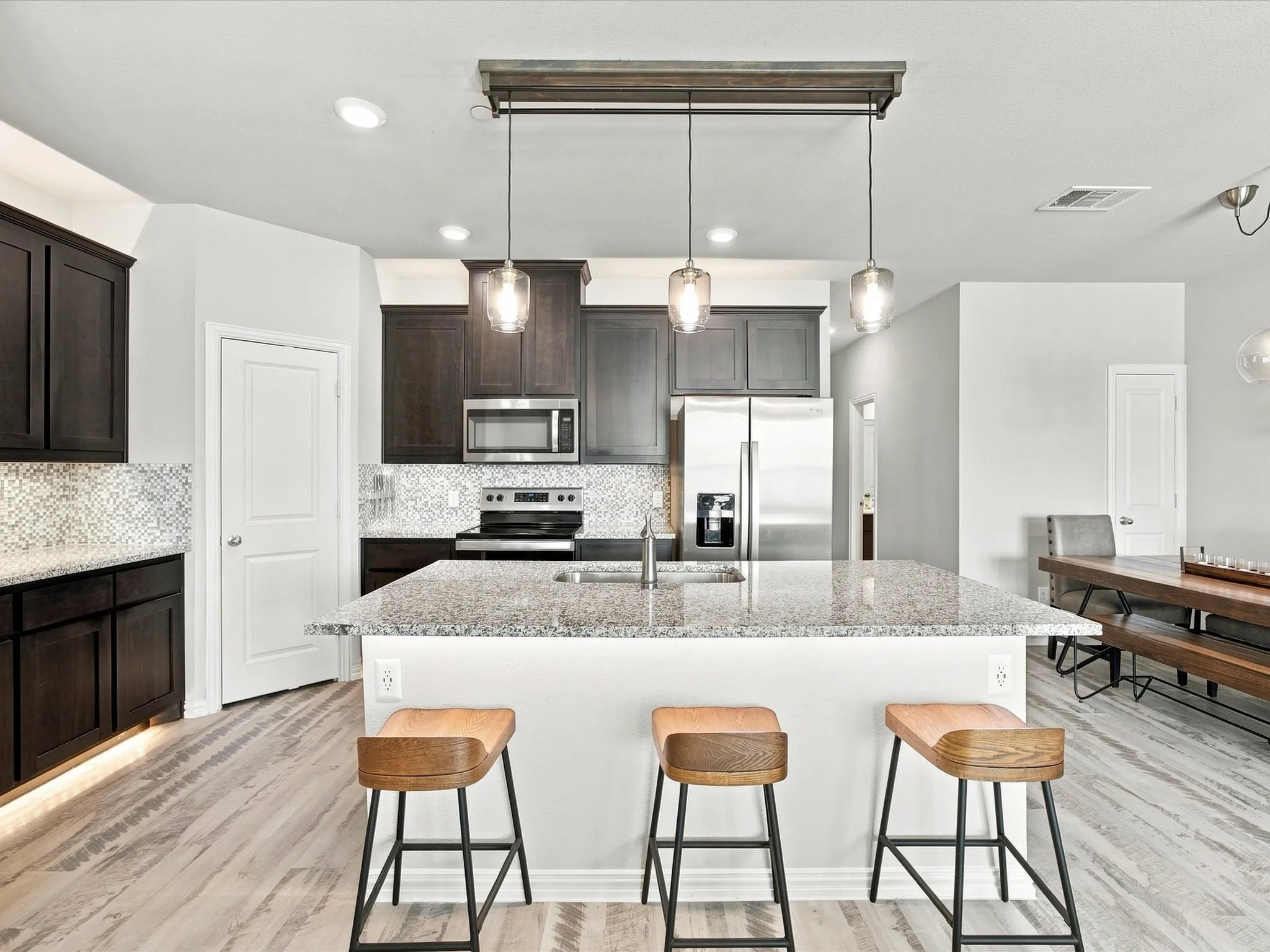 Kitchen featuring a large island with stone countertop, dark wood-finish cabinetry, patterned tile backsplash, stainless steel appliances, and wood-finish flooring