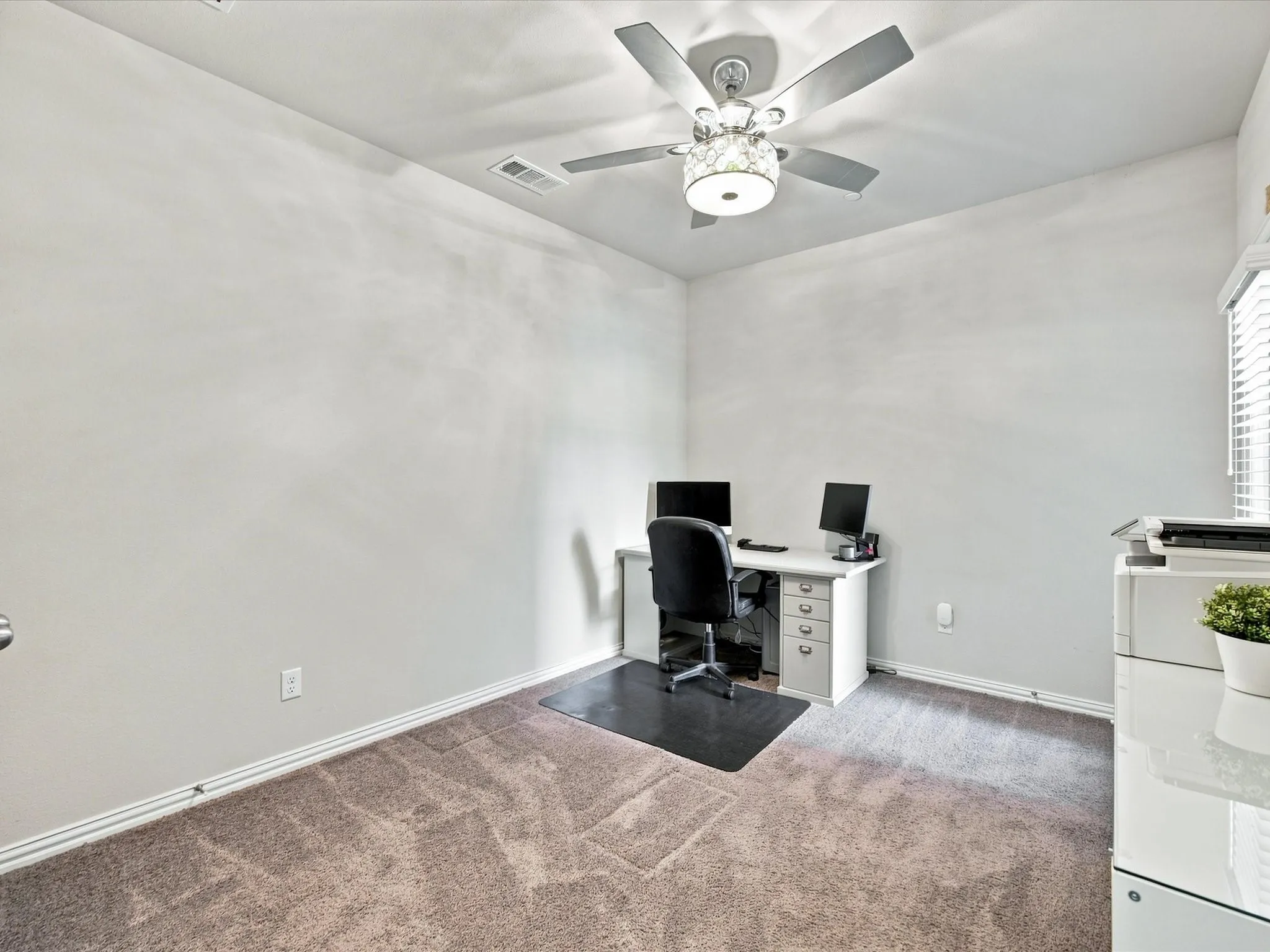 Neutral wall paint, ceiling fan with integrated lighting, window with horizontal blinds, and carpeted flooring