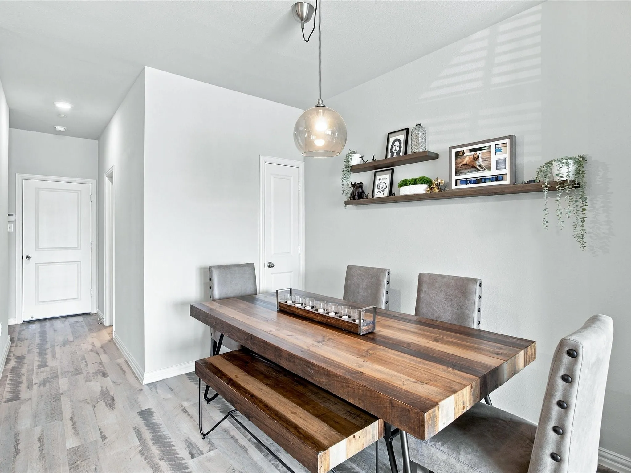 Dining area featuring wood-finish flooring, a contemporary pendant light fixture, and two wall-mounted floating shelves