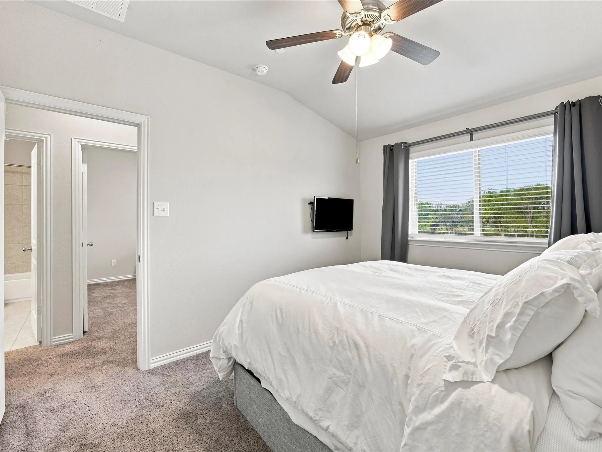 Vaulted ceiling, ceiling fan with light fixture, window with blinds, carpeted flooring, and a white interior door frame