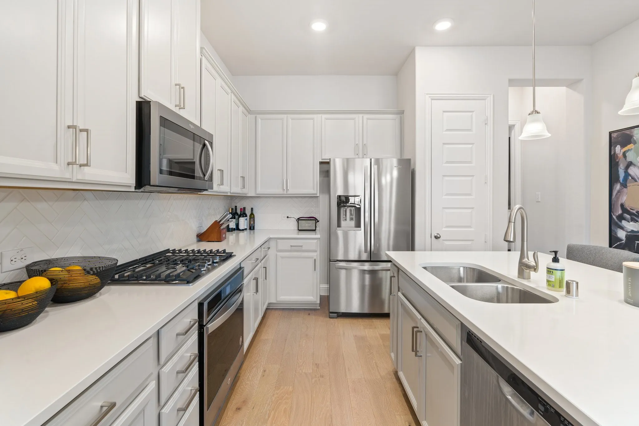 Kitchen featuring stainless steel appliances, sink, backsplash, light wood-type flooring, and white cabinetry