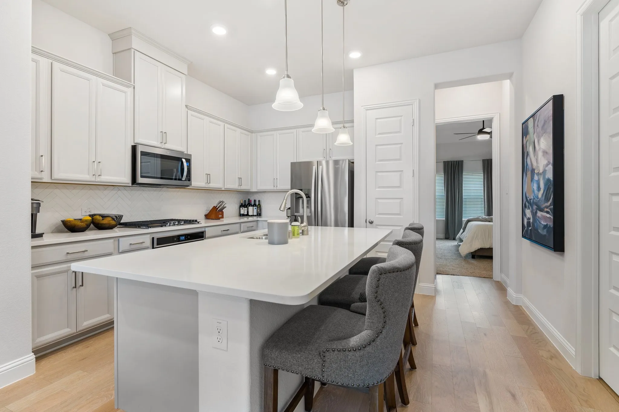 Kitchen with light hardwood / wood-style flooring, stainless steel appliances, decorative light fixtures, decorative backsplash, and an island with sink