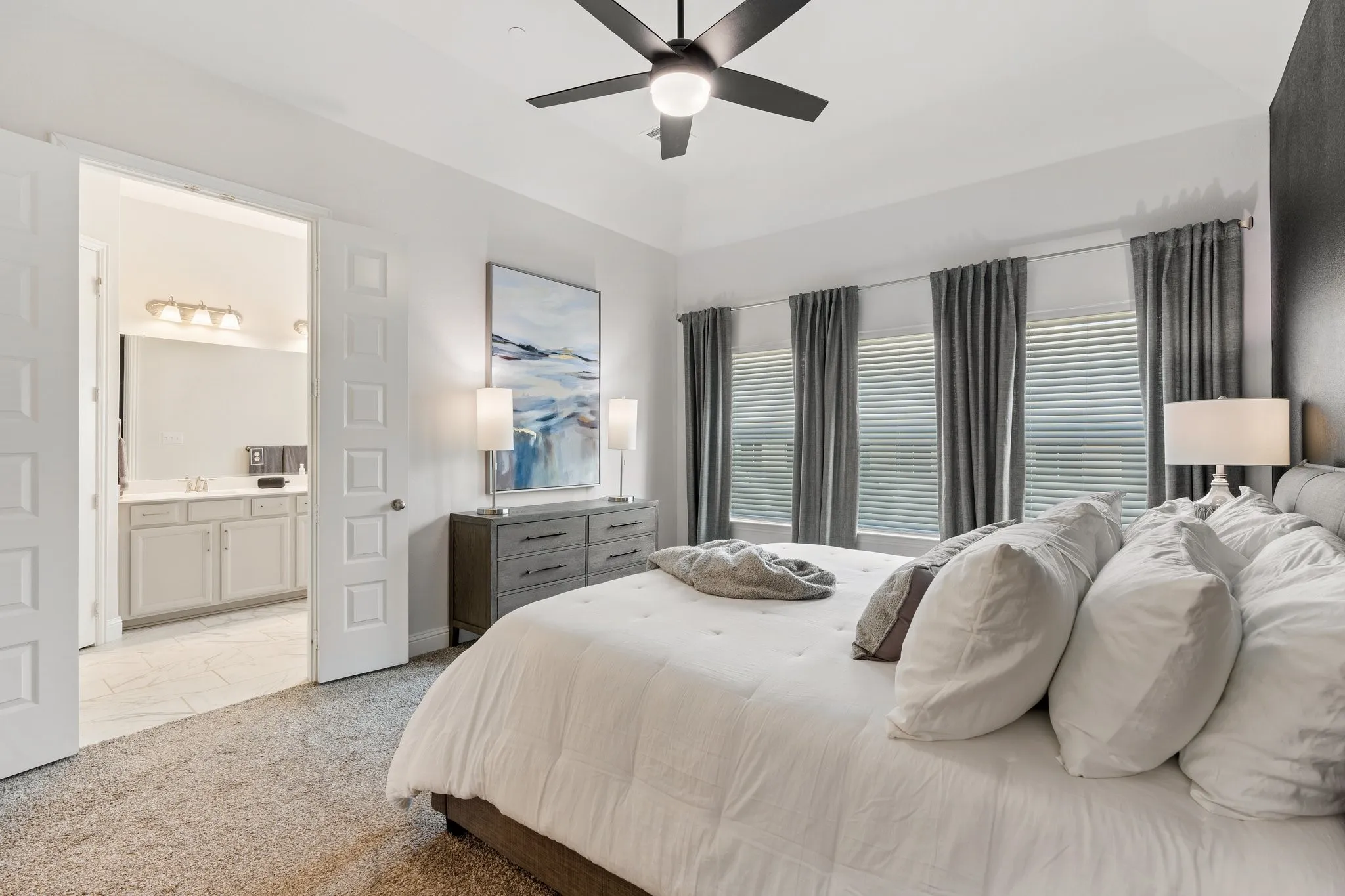 Carpeted bedroom with sink, ensuite bathroom, ceiling fan, and a tray ceiling