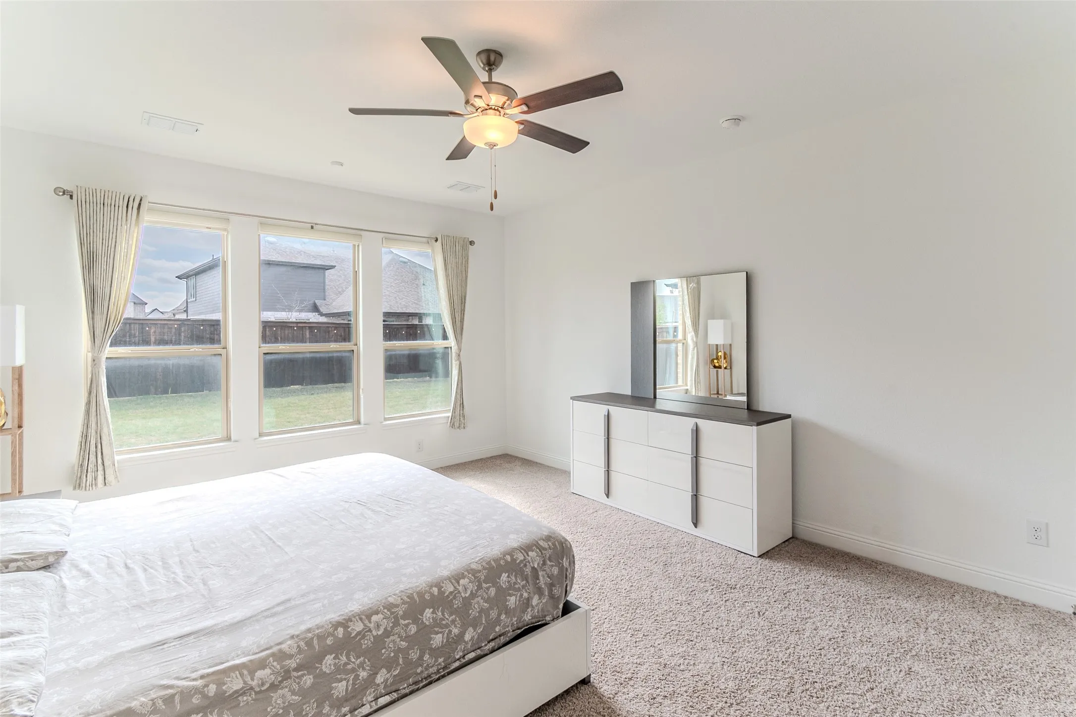 Wall-to-wall carpeting, three large windows with roller shades, and a ceiling fan with integrated lighting