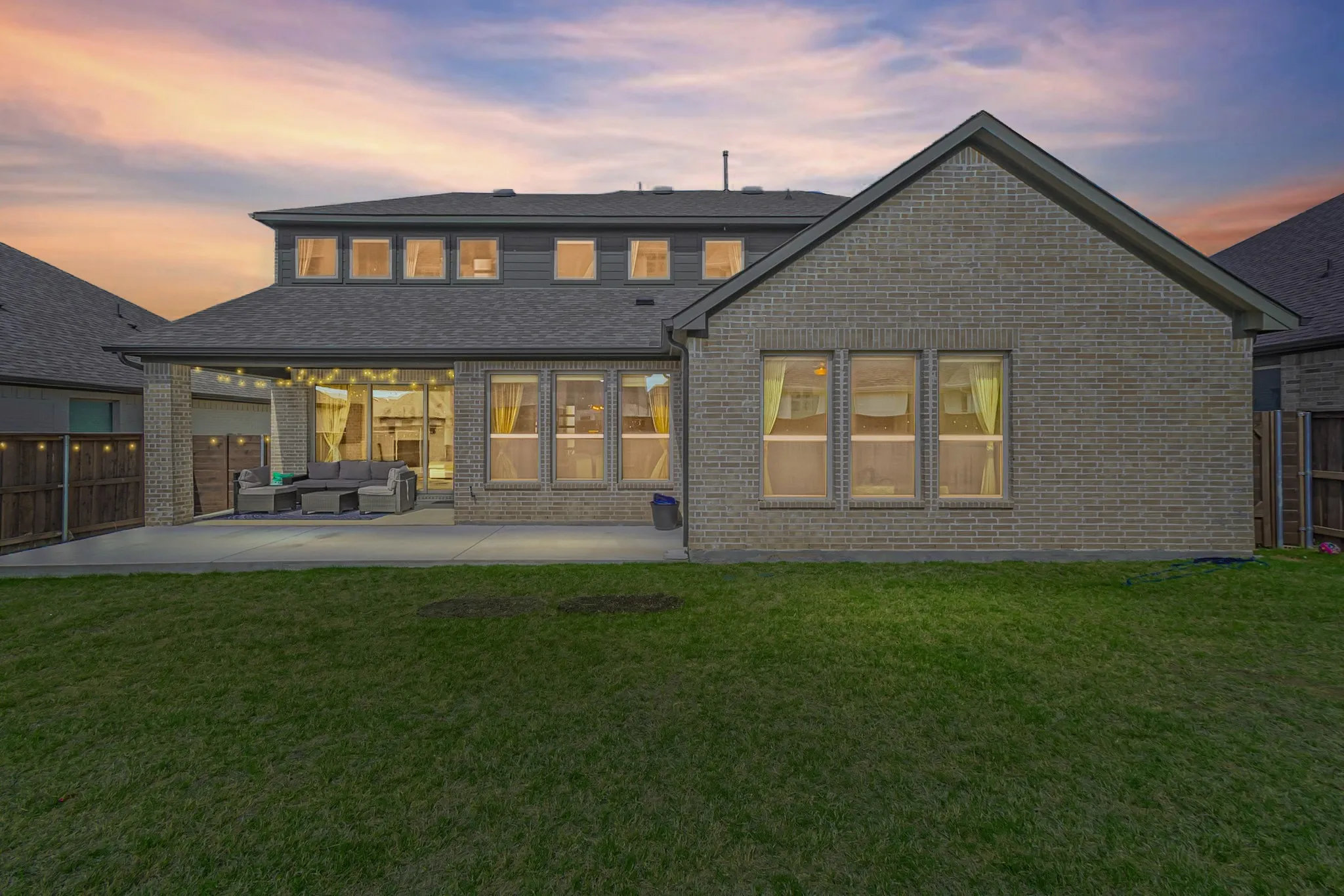 Expansive backyard with a manicured lawn, concrete patio, covered outdoor living space, and a brick and siding exterior