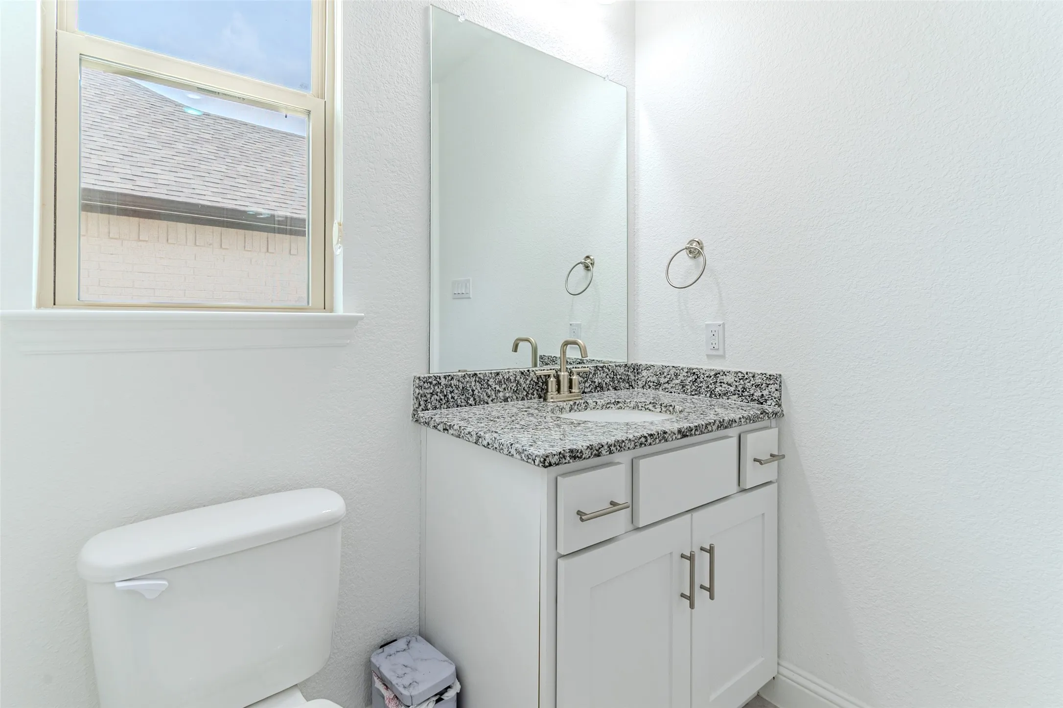 White vanity with a speckled countertop, a mirrored wall, and a single window