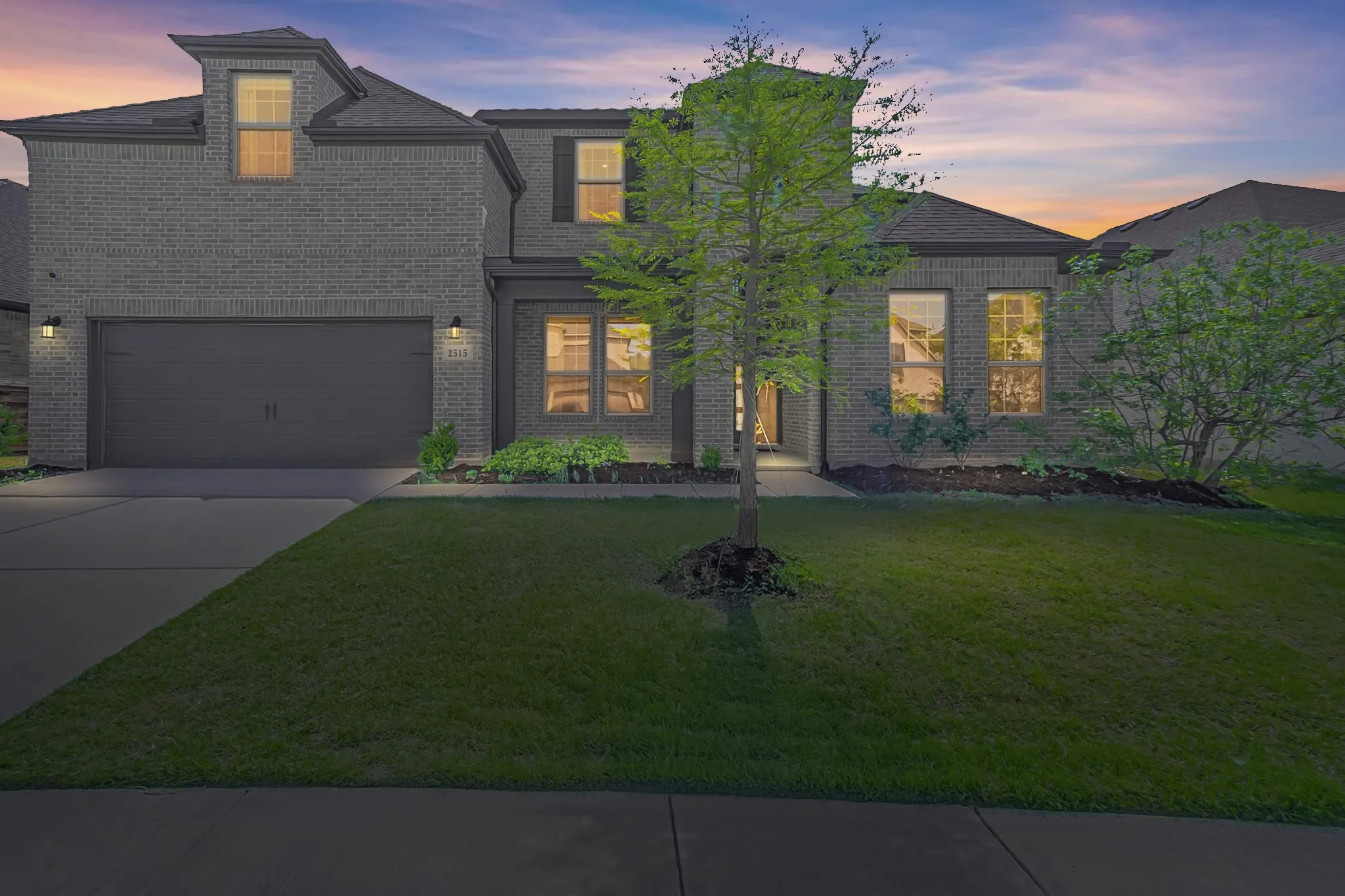 Two-story residence featuring brick exterior, attached two-car garage, front yard with mature landscaping, and an inviting entryway