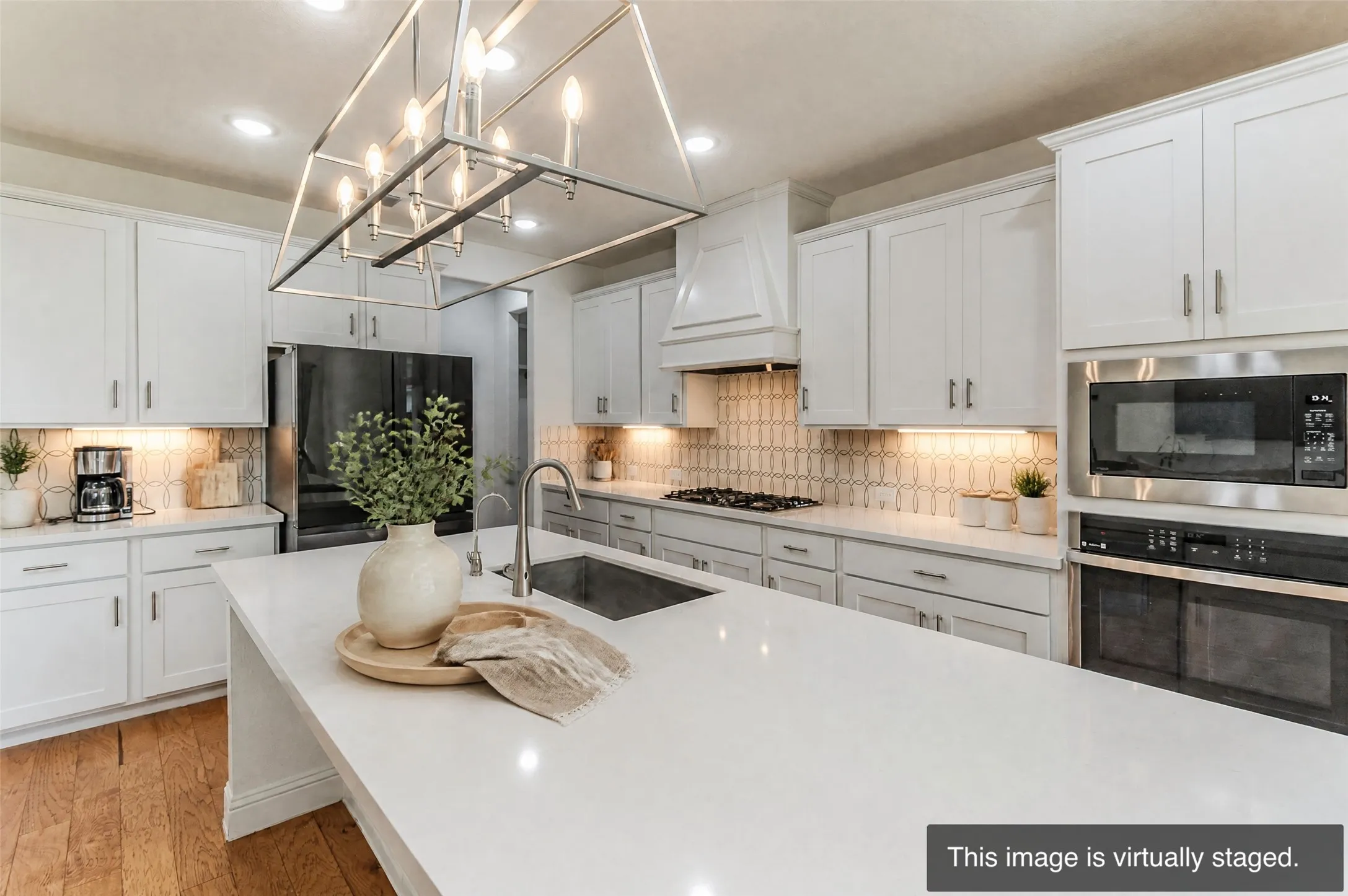 Kitchen featuring white shaker cabinetry, stainless steel appliances, a center island with an undermount sink, a geometric tile backsplash, and wood-finish flooring