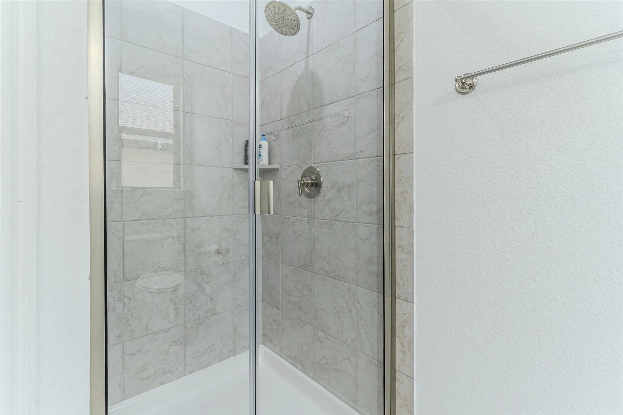 Tiled shower with a rain shower head, built-in shelving, and a glass enclosure