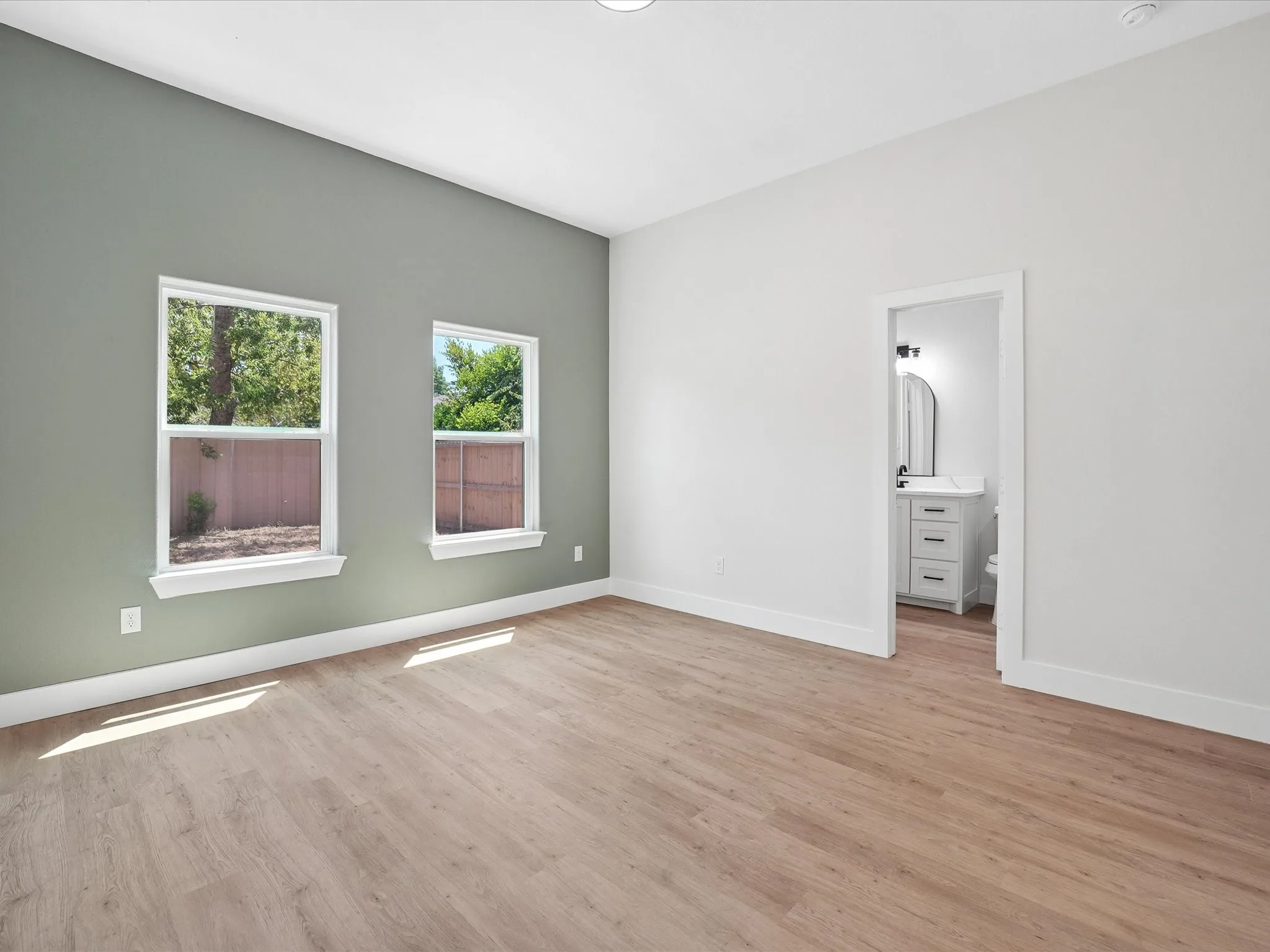Wood-finish flooring, high ceilings, multiple windows, and a dedicated entry to a bathroom featuring a vanity with drawer storage and a rounded mirror